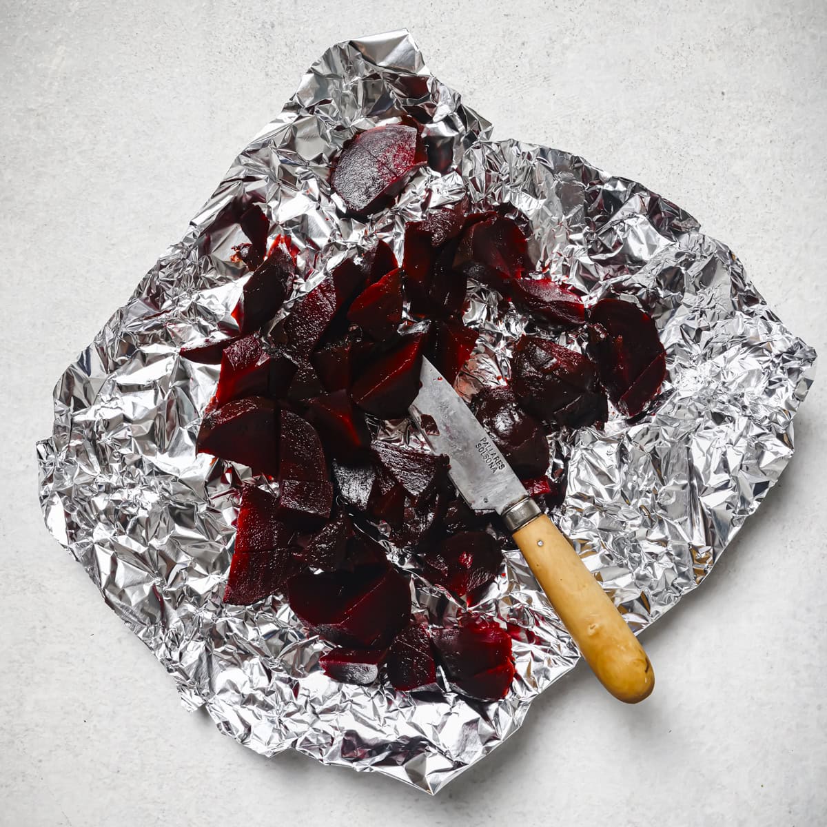 a knife and chopped cooked beets on a piece of aluminum foil.