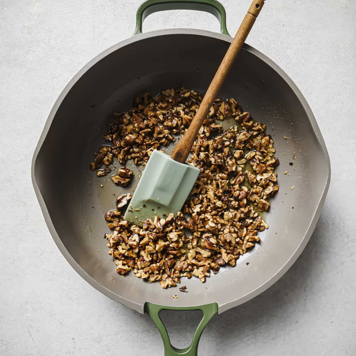 a silicone spatula and chopped walnuts cooking in a frying pan.
