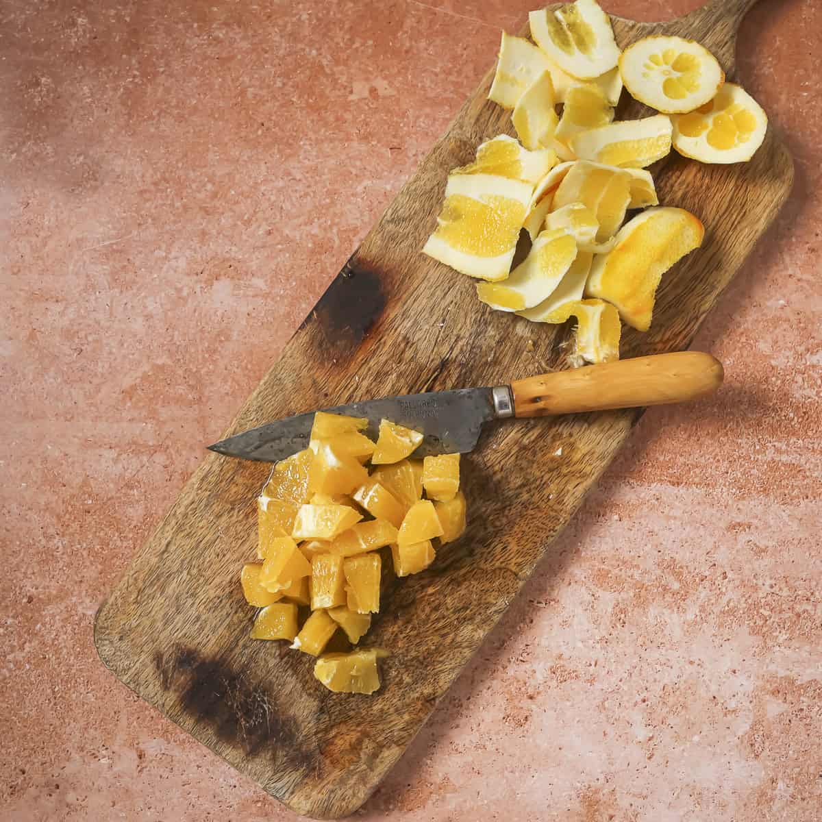 small orange pieces and a pairing knife next to a pile of the pith on a wooden cutting board.