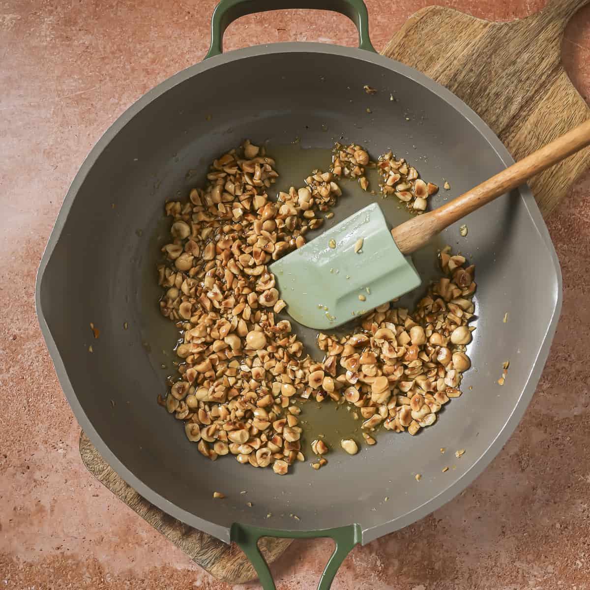 olive oil and chopped hazelnuts in a frying pan with a silicone spatula.
