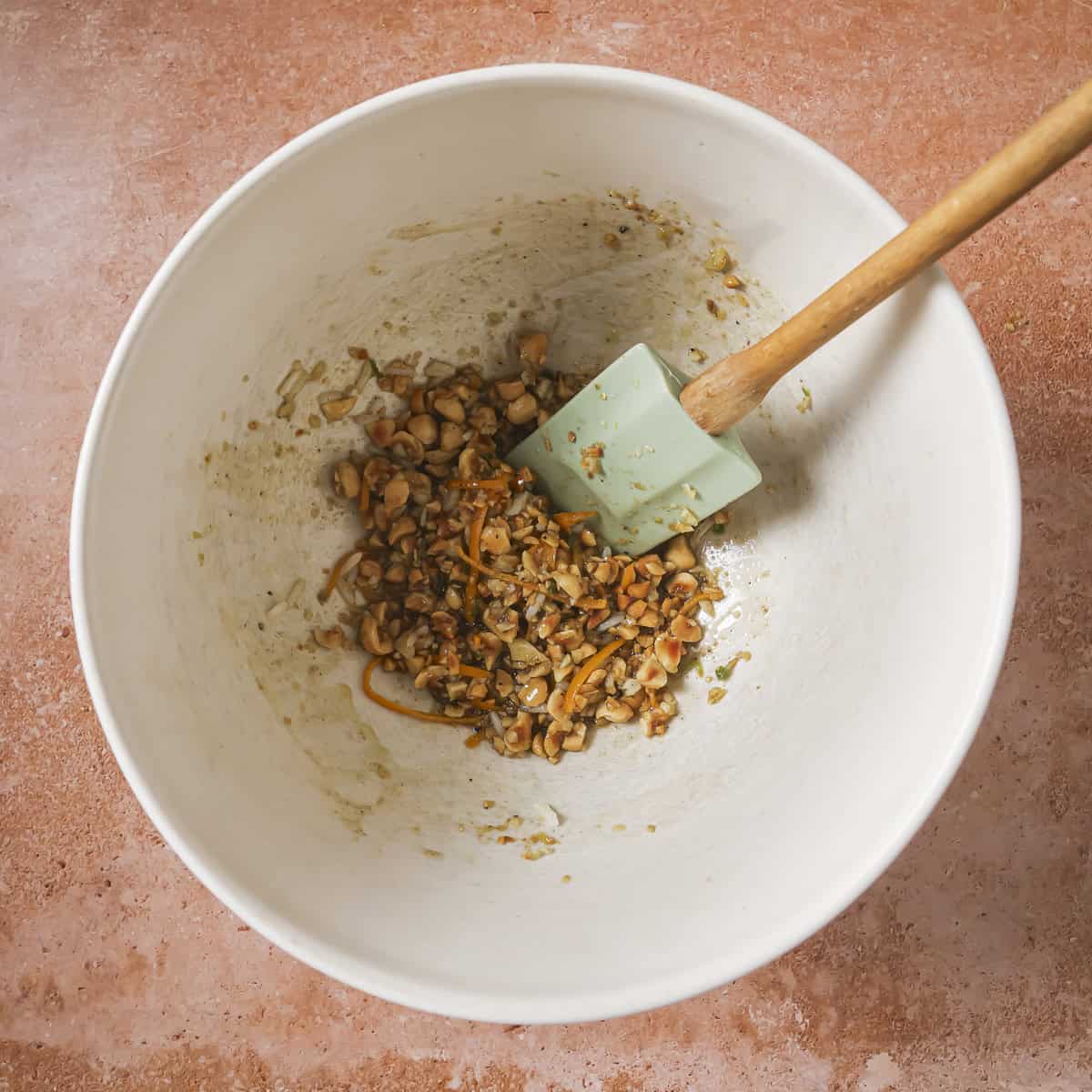 serrano, spices, salt and pepper added to hazelnut, garlic and orange mixture in a bowl with a silicone spatula.