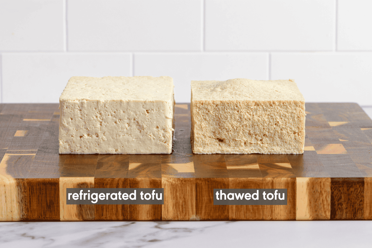 a block of refrigerated tofu next to a block of thawed tofu on a wooden cutting board.
