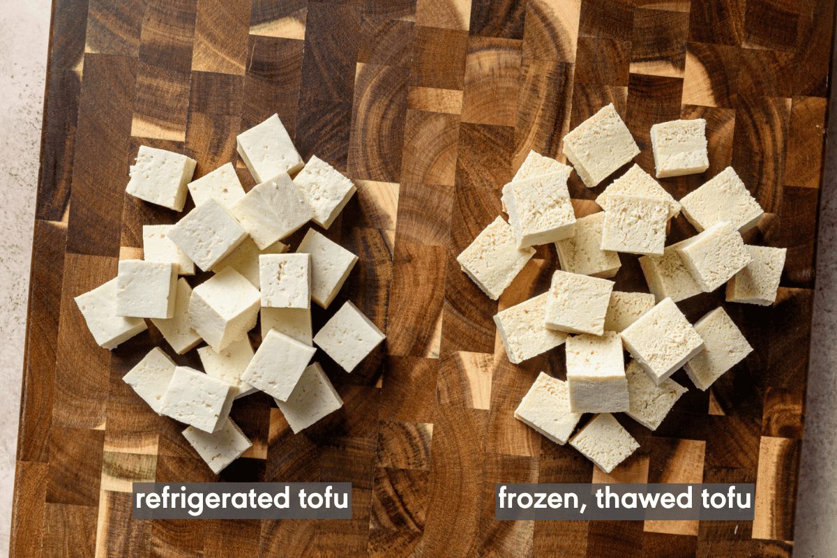 a pile of cubes of refrigerated tofu next to a pile of cubes of frozen, thawed tofu on a wooden cutting board.