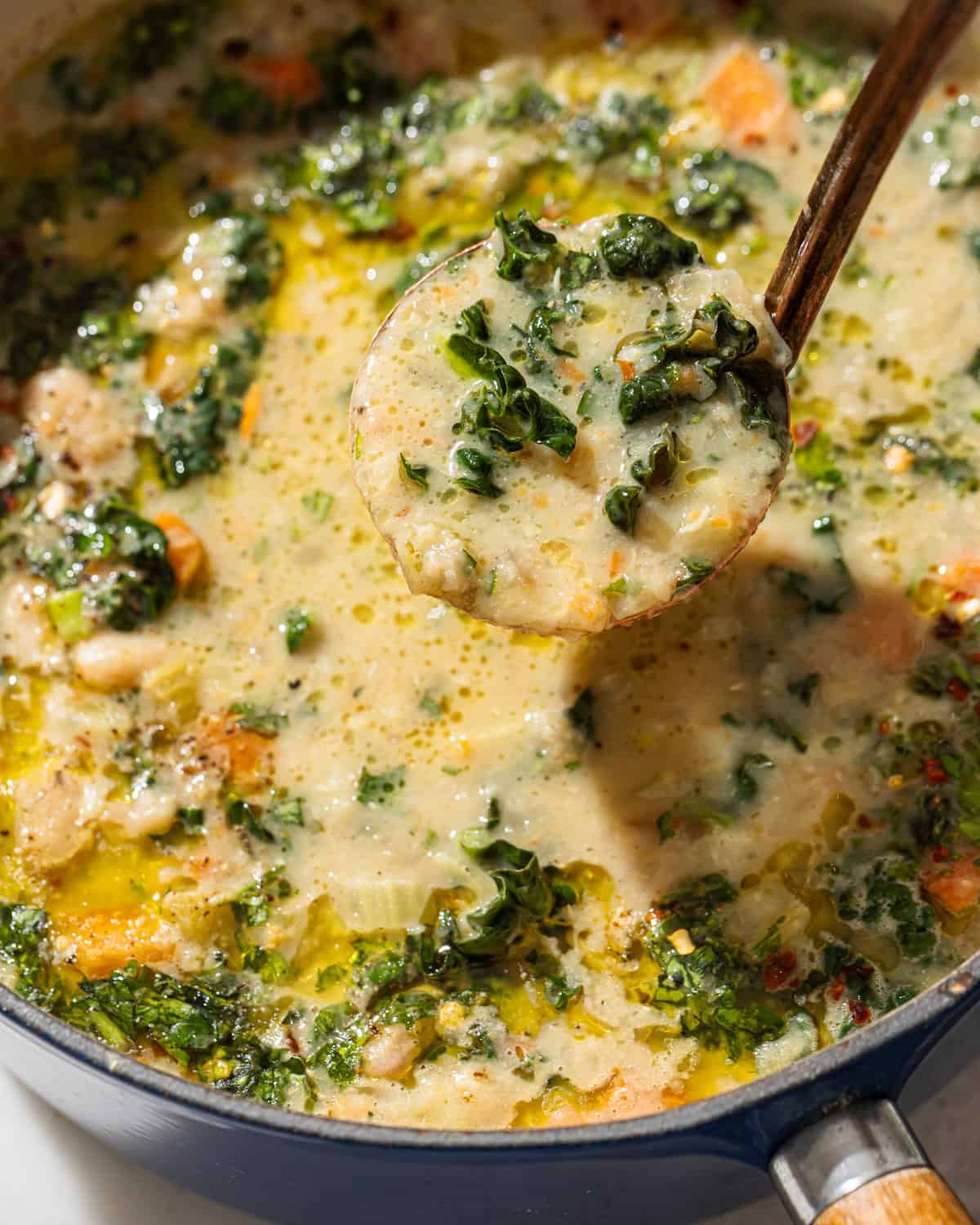 a ladle full of white bean kale soup being held above the full pot.
