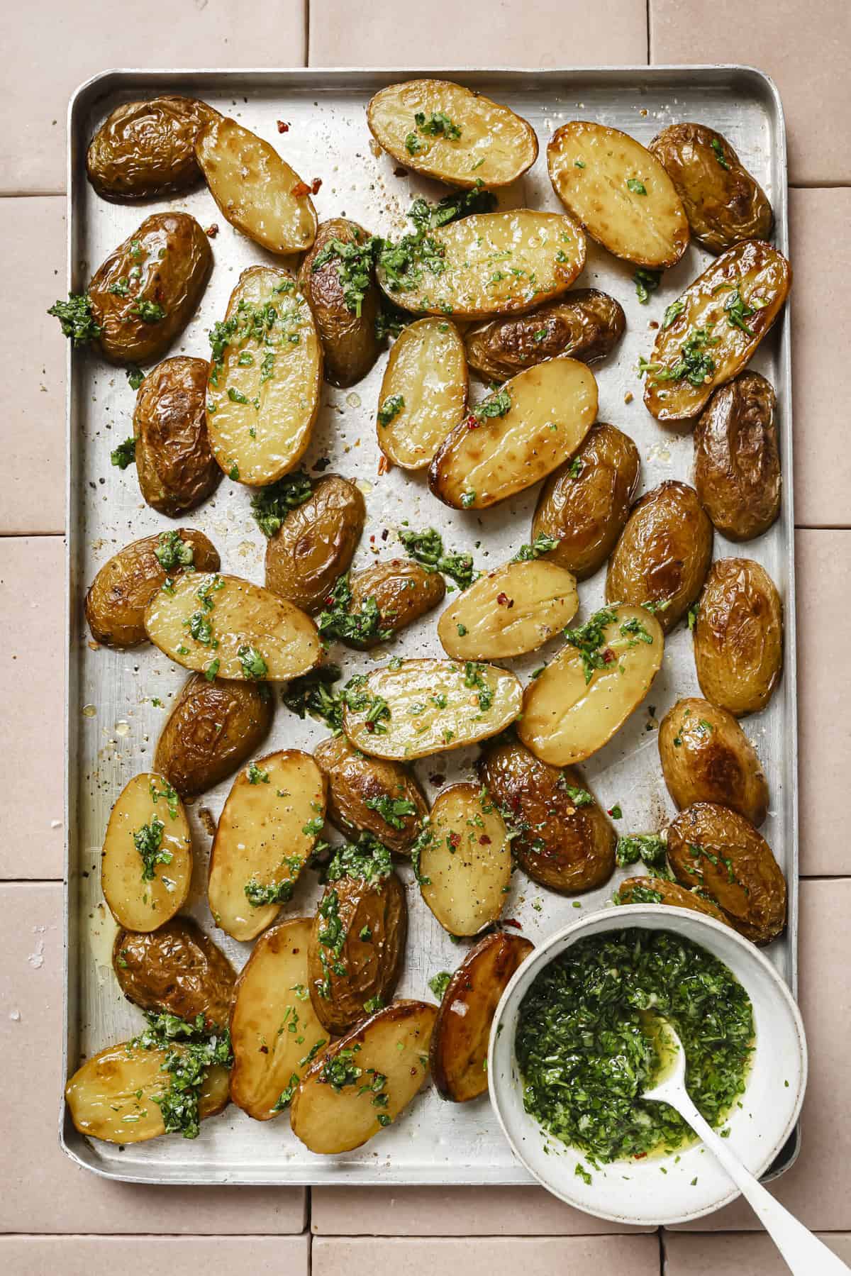small bowl of gremolata and roasted potatoes covered in gremolata on a sheet pan.