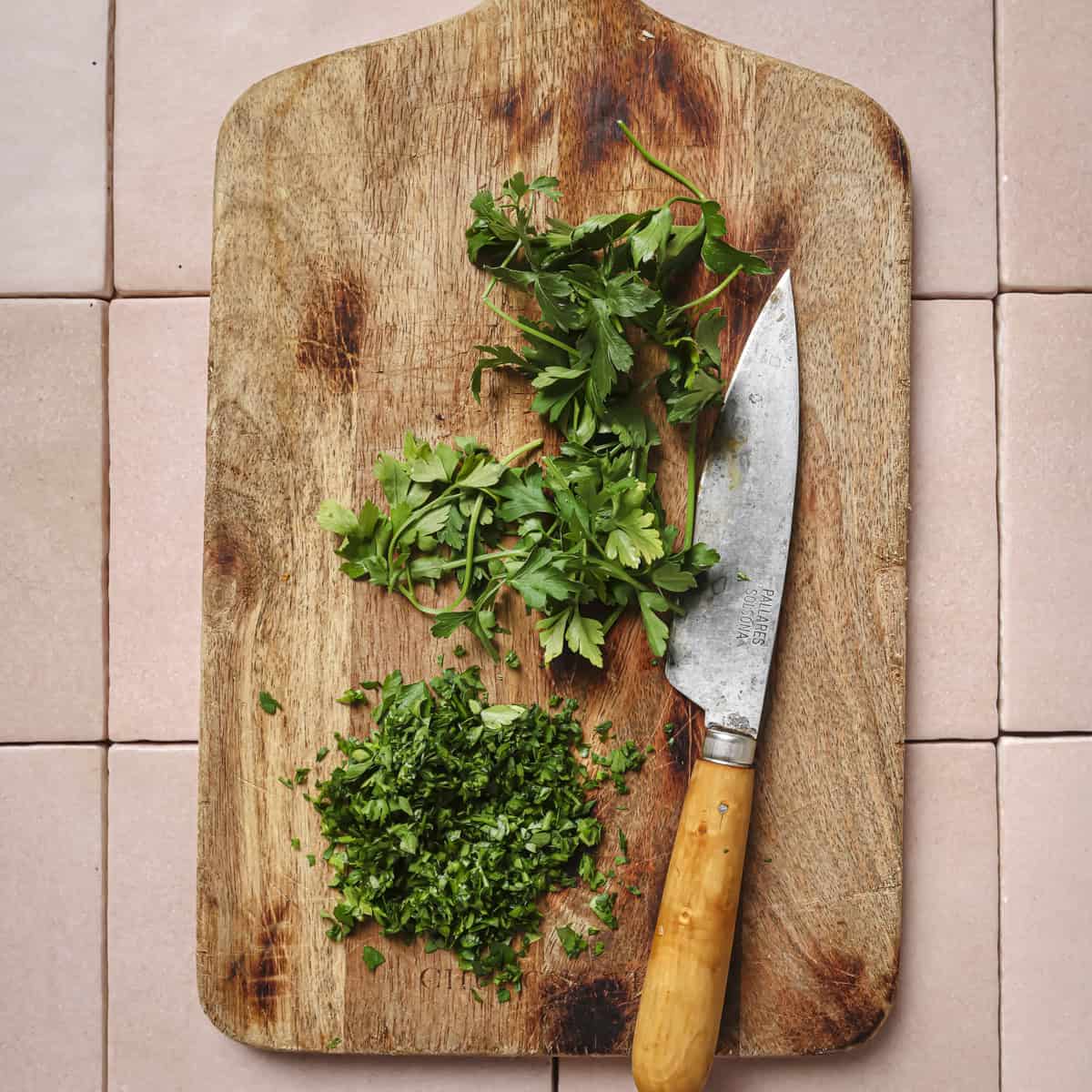 chopped parsley and a knife on a wooden cutting board.