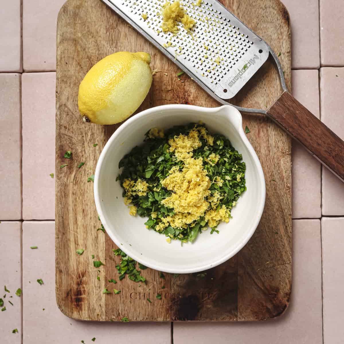 parsley and lemon zest in a small bowl on a wooden cutting board.