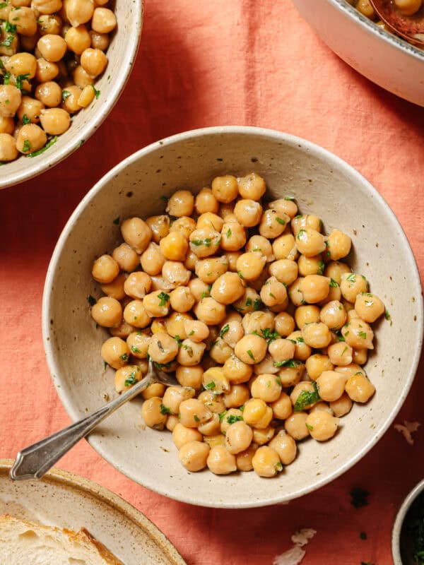overhead view of cooked chickpeas with parsley in a bowl with a silver spoon in it.
