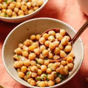 person holding deep serving spoon filled with cooked chickpeas over a bowl of the chickpeas.