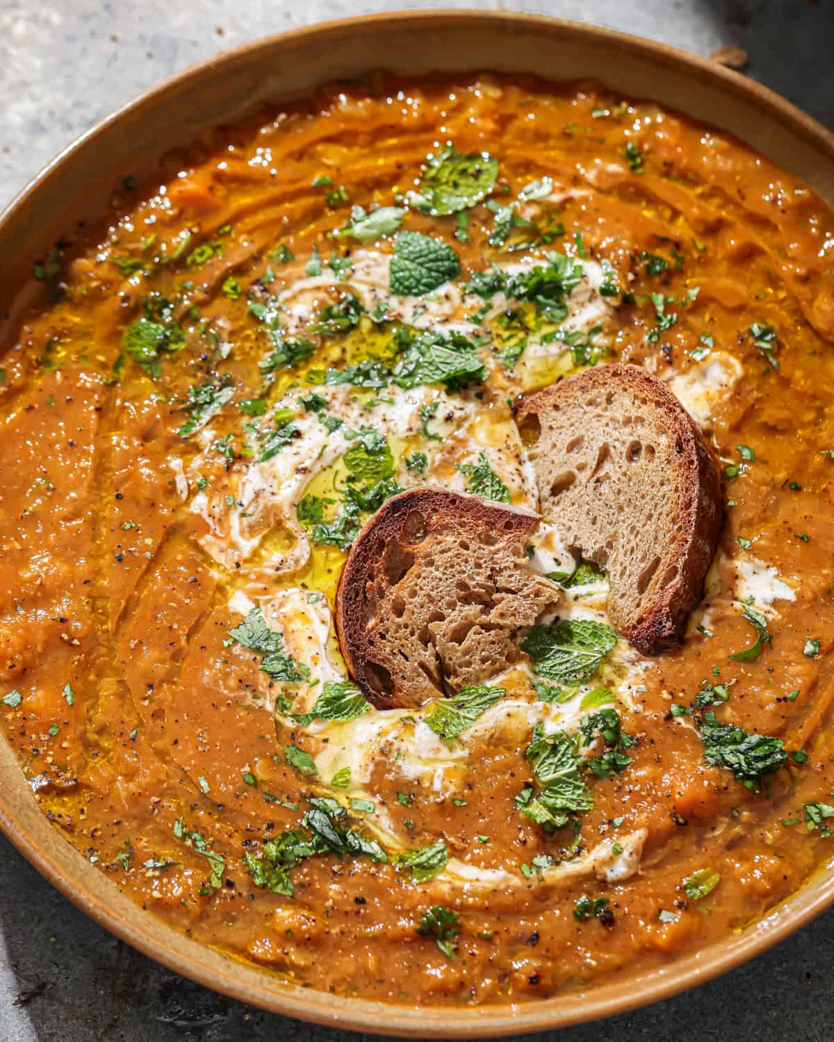 Close up overhead photo of a bowl of soup with bread in it garnished with coconut yogurt and fresh herbs.