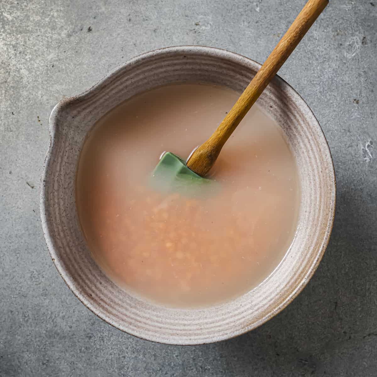 lentils soaking in a bowl of water with a silicone spatula in it.
