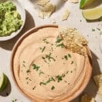 overhead view of a bowl of queso topped with cilantro on a table.