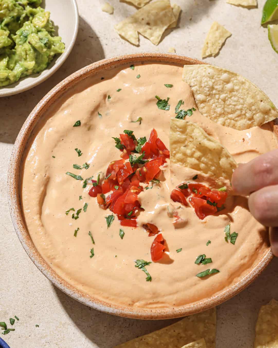 person dipping a tortilla chip into a bowl of queso.