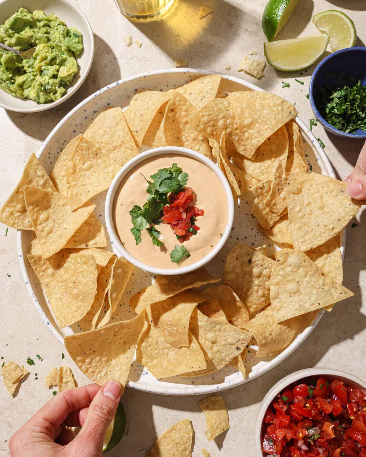 person taking a chip from a plate with chips and a bowl of queso on it.