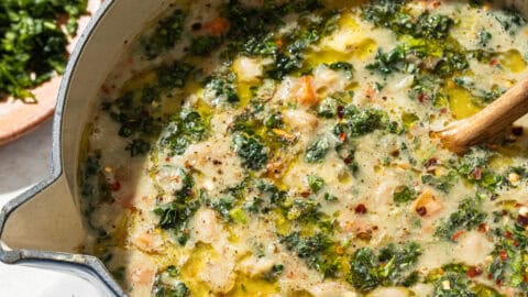 a blue pot of white bean soup with kale on a white surface.