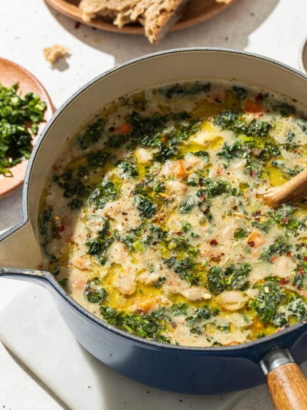 a blue pot of white bean soup with kale on a white surface.