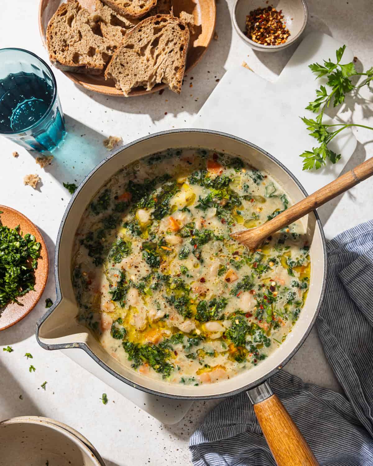 overhead view of a table with a plate of bread, full pot of soup, ingredient bowls and glass of water.