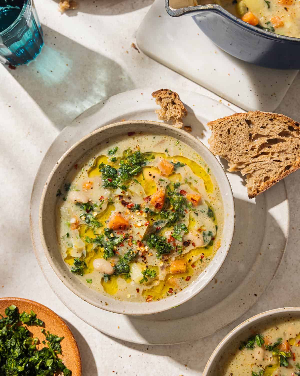 bowl of white bean soup next to a chunk of crusty bread on a table.