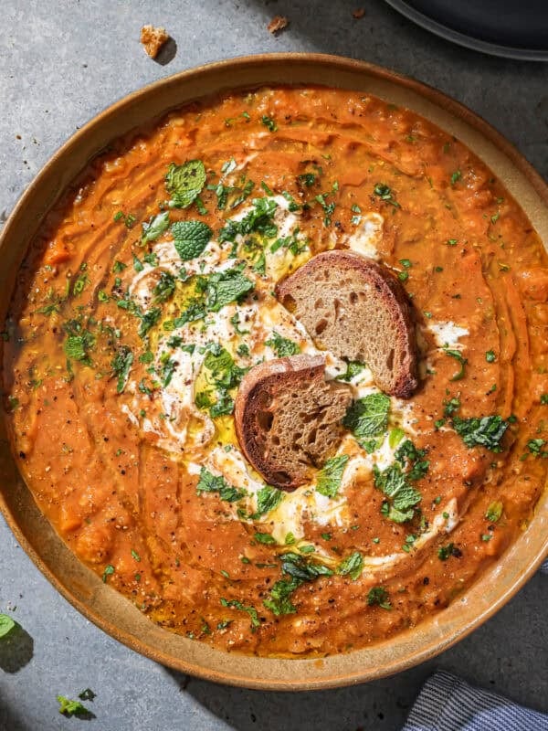 Bowl of red lentil soup soup with bread in it topped with yogurt and fresh herbs.