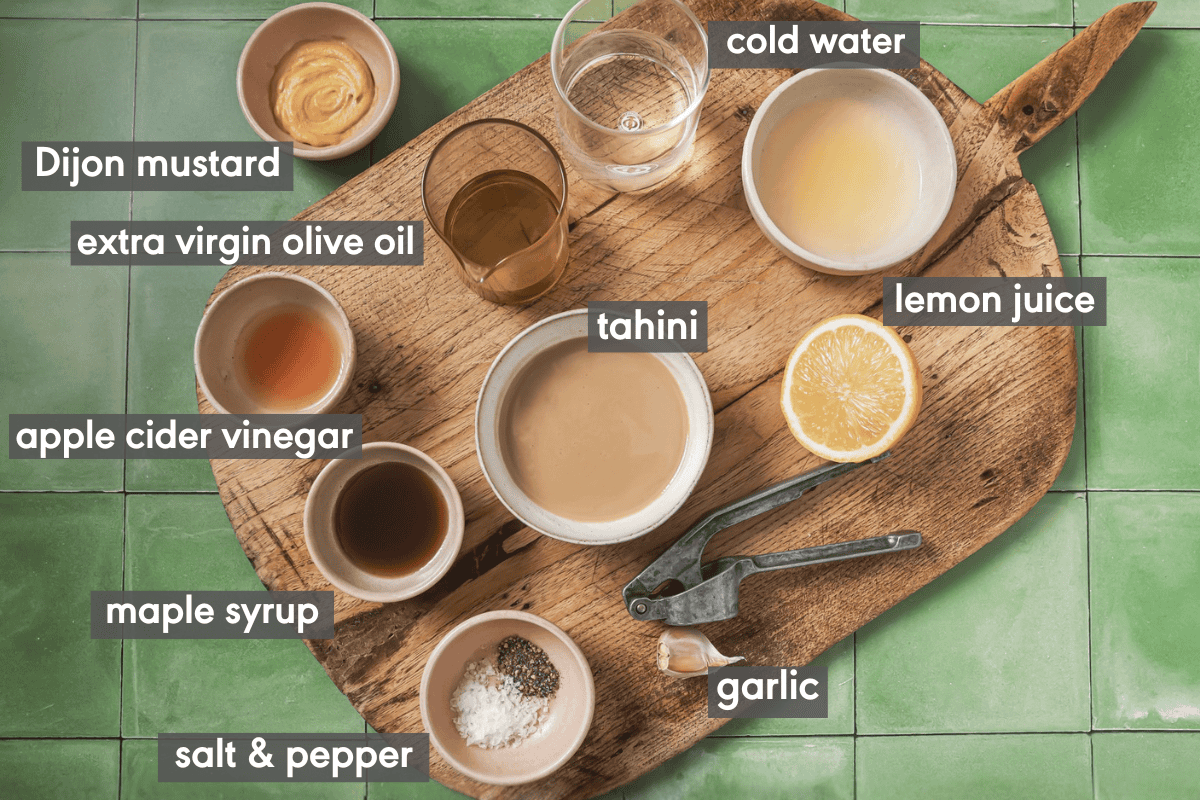 ingredients for tahini dressing in various small bowls on a wooden cutting board.