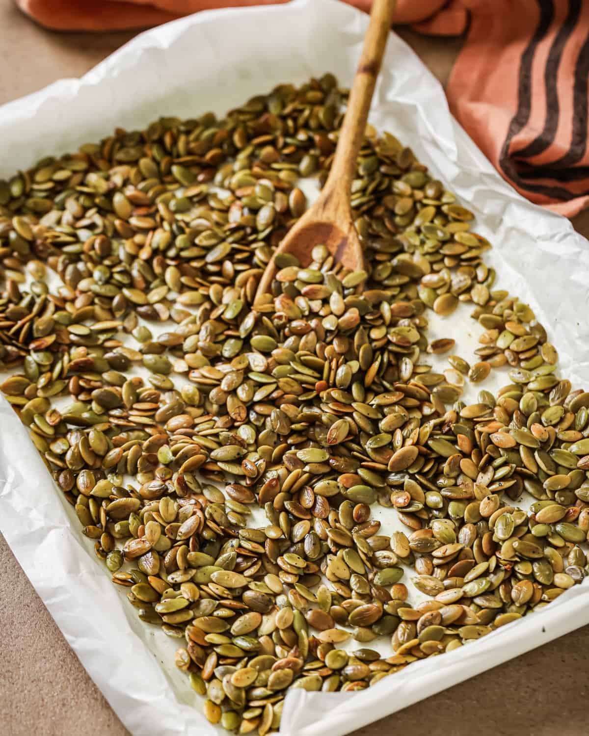 Roasted pepitas and a wooden spoon on a baking tray lined with parchment paper.