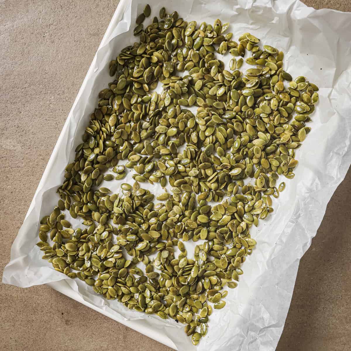 unroasted pepitas on a parchment paper lined sheet pan.