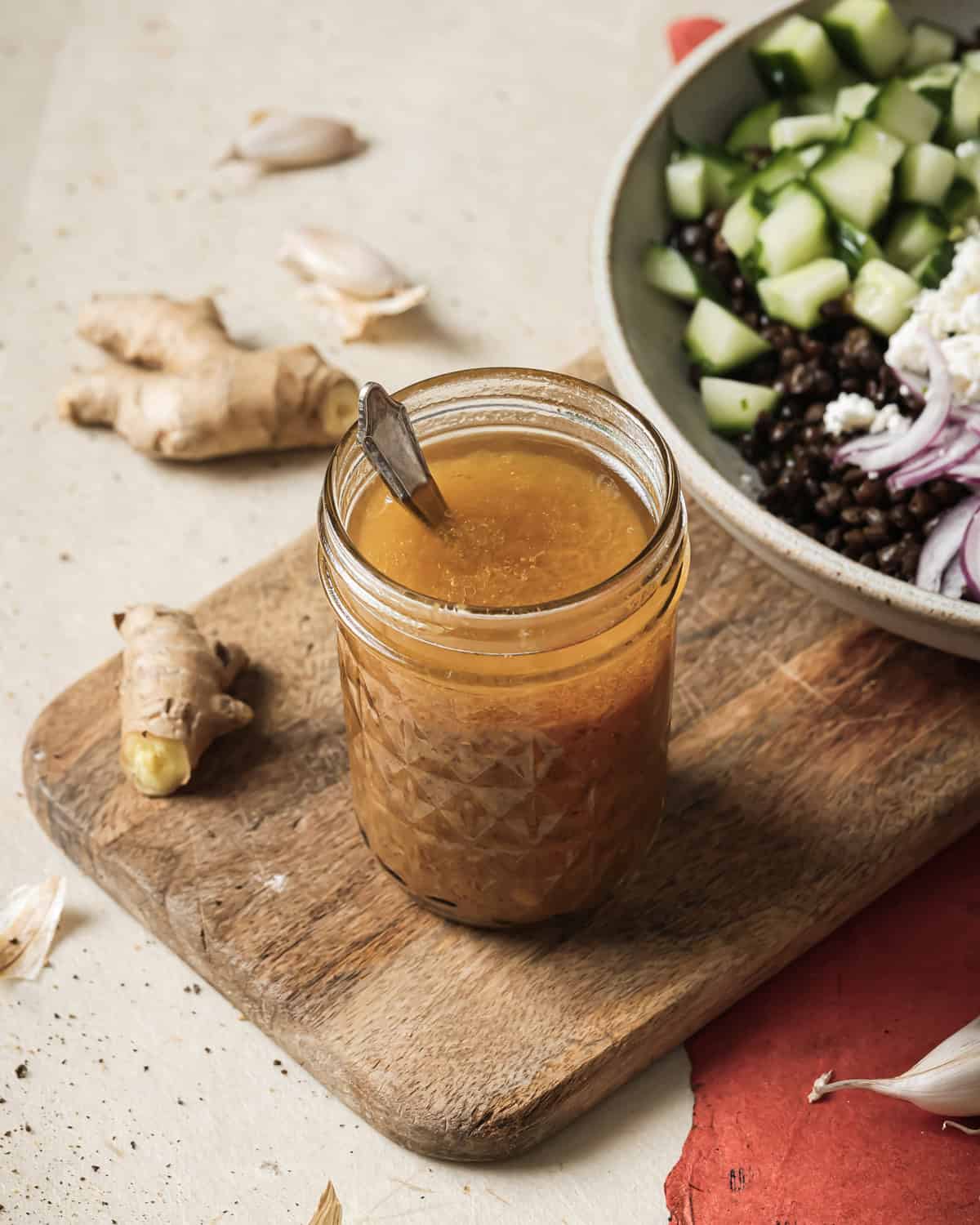 Sesame miso dressing in a small mason jar and a bowl of salad on a wooden serving board.