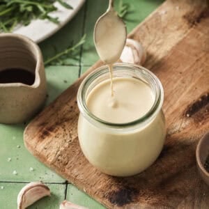 person removing spoon from jar of tahini dressing on a wooden cutting board.