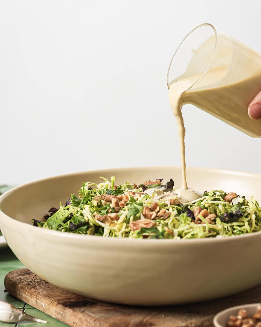 side view of person pouring tahini dressing onto salad in a bowl.