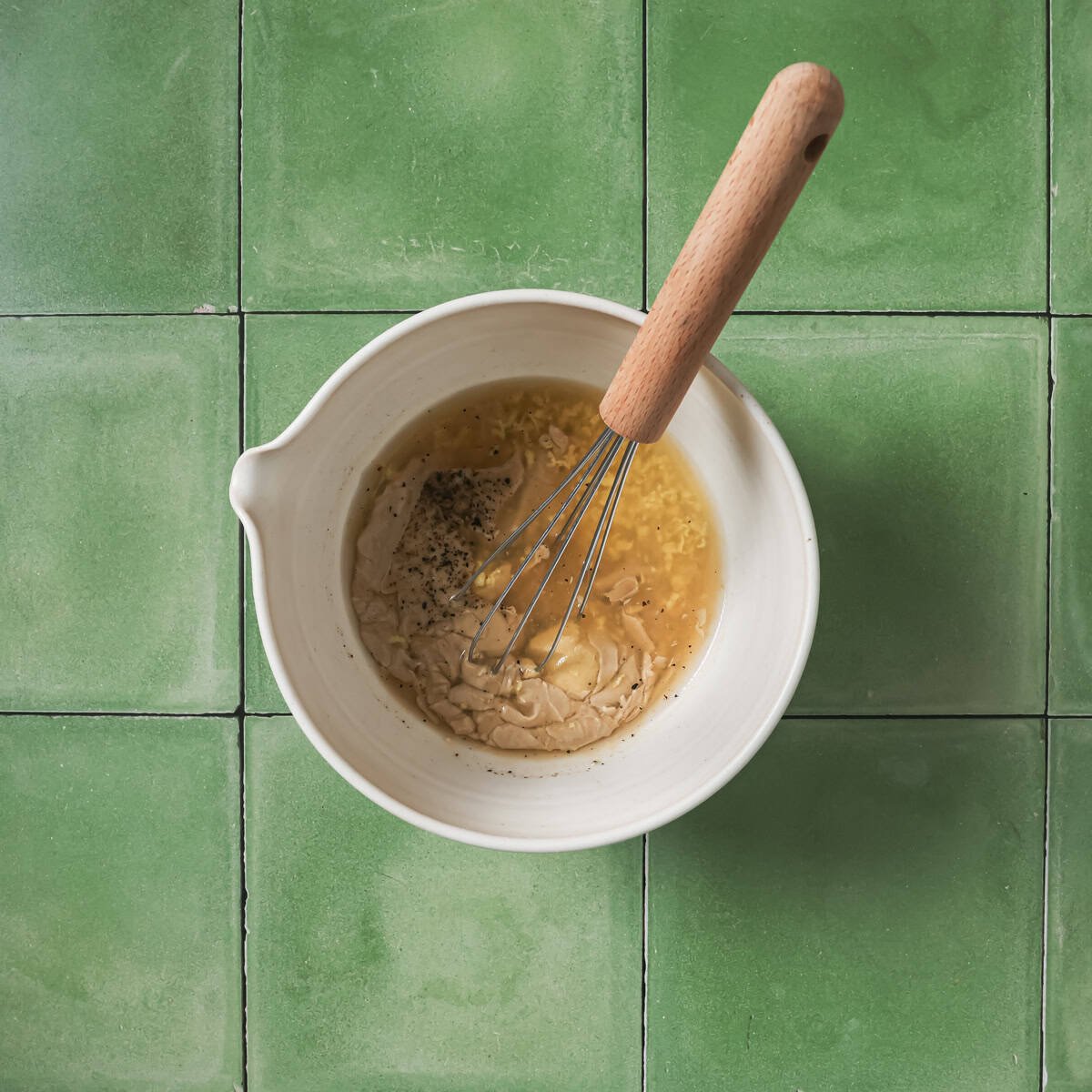Lemon juice, vinegar, tahini, mustard, garlic, maple syrup, salt, and pepper in a bowl with a whisk.
