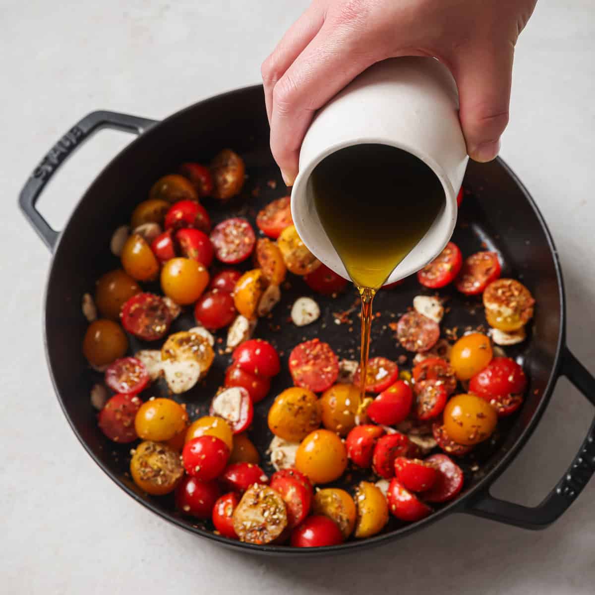 person pouring olive oil over the tomatoes.