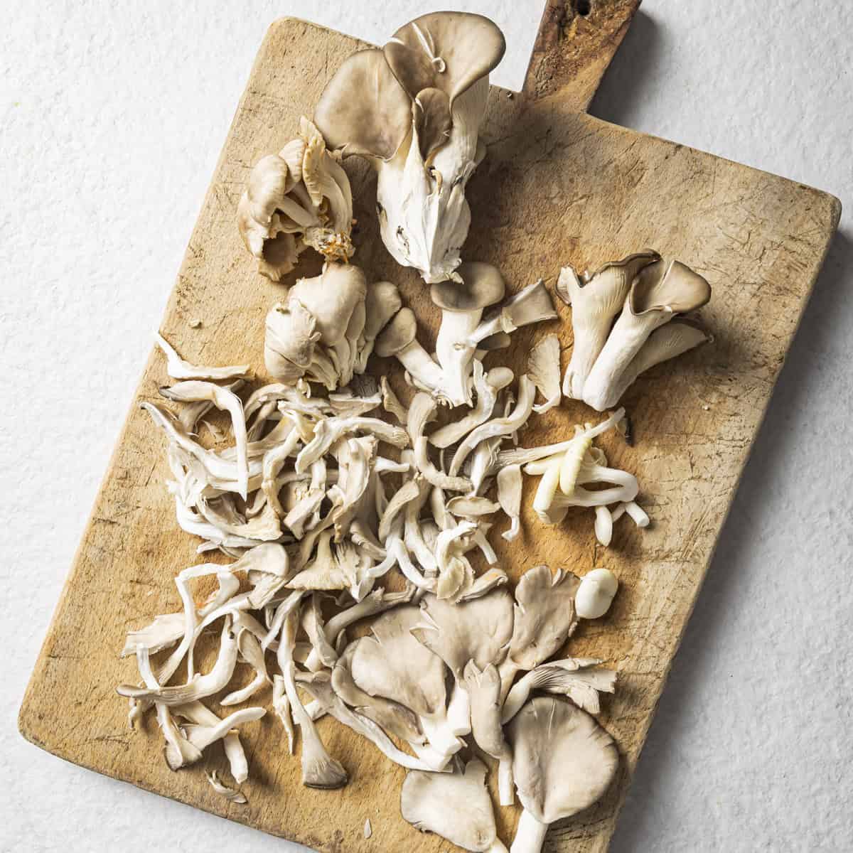 torn mushrooms on a wooden cutting board.