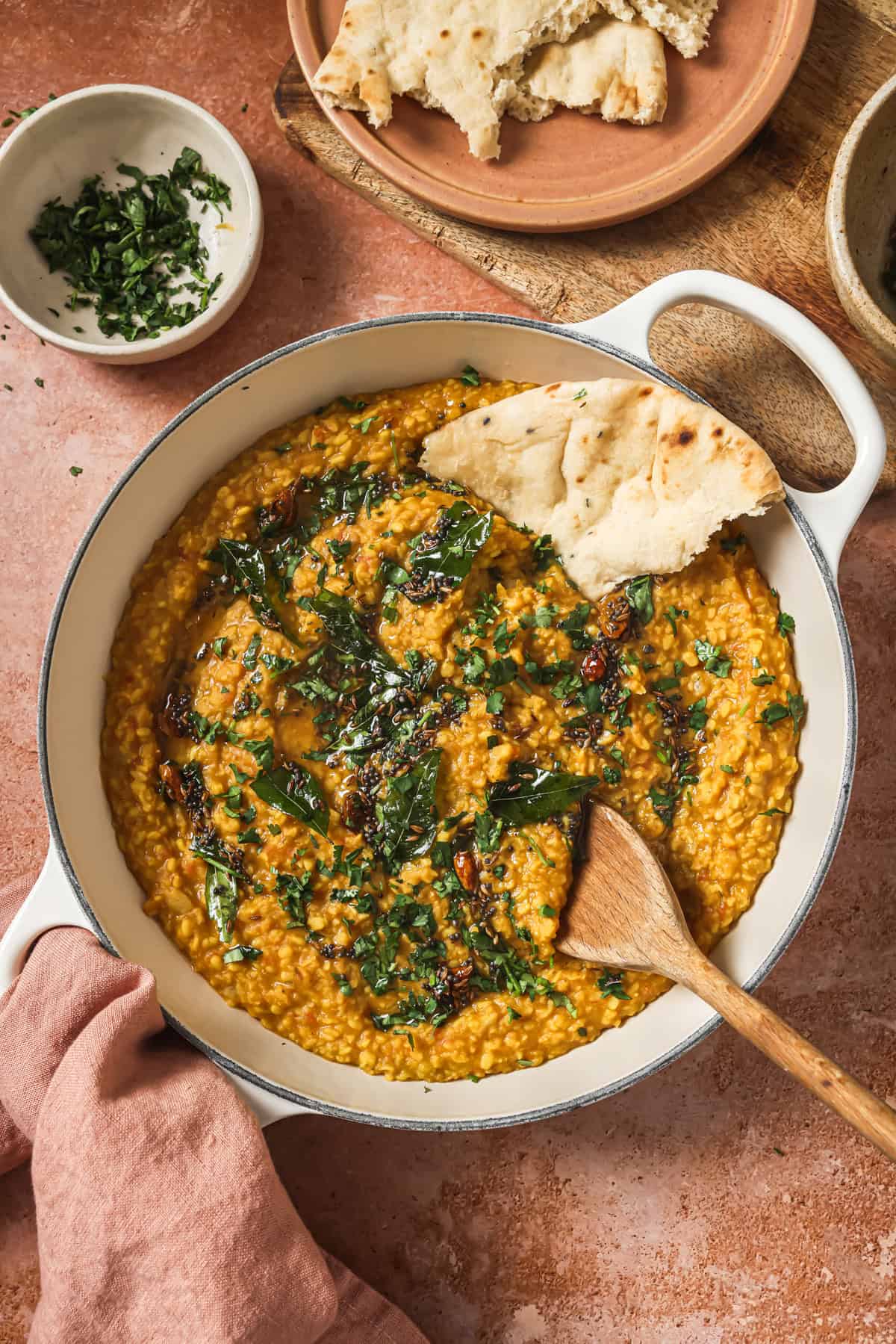 overhead view of deep skillet of dal tadka with a piece of naan in it.