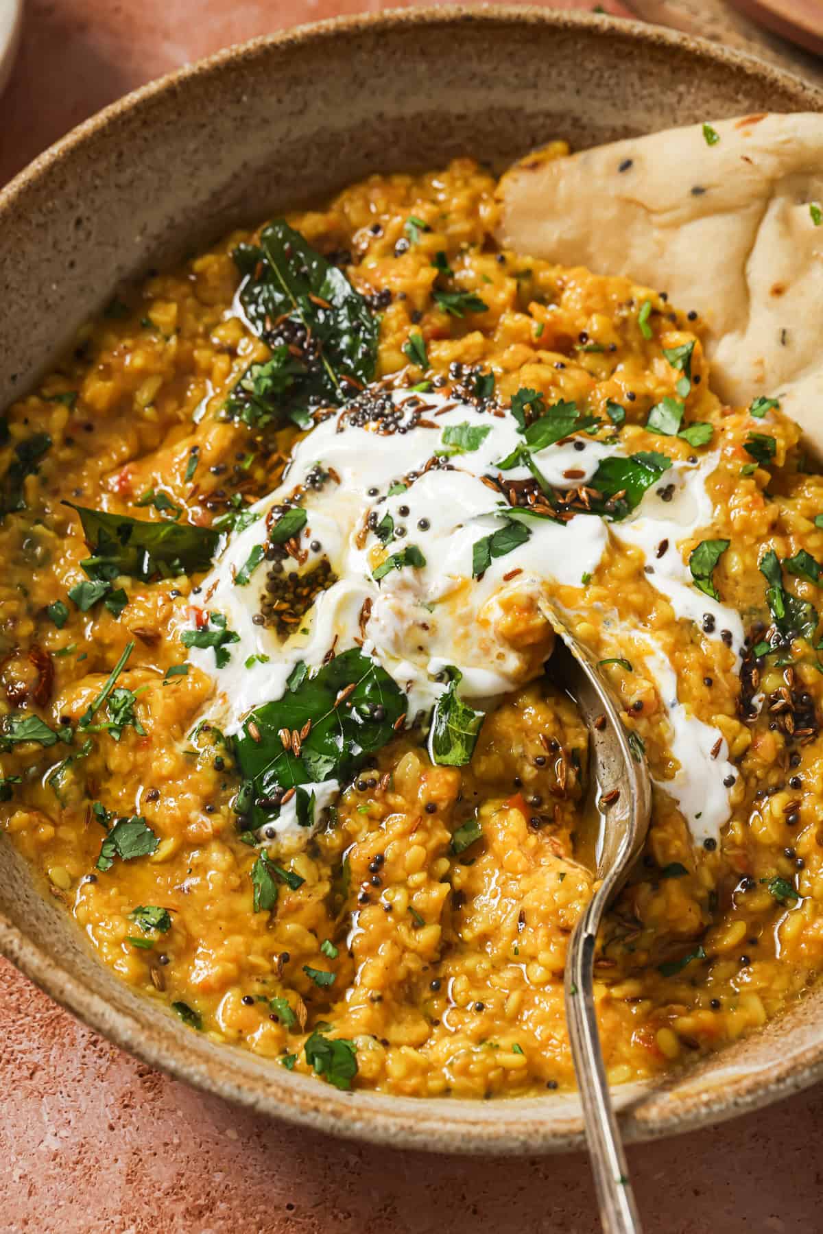 close up of bowl of dal tadka with yogurt and a piece of naan.