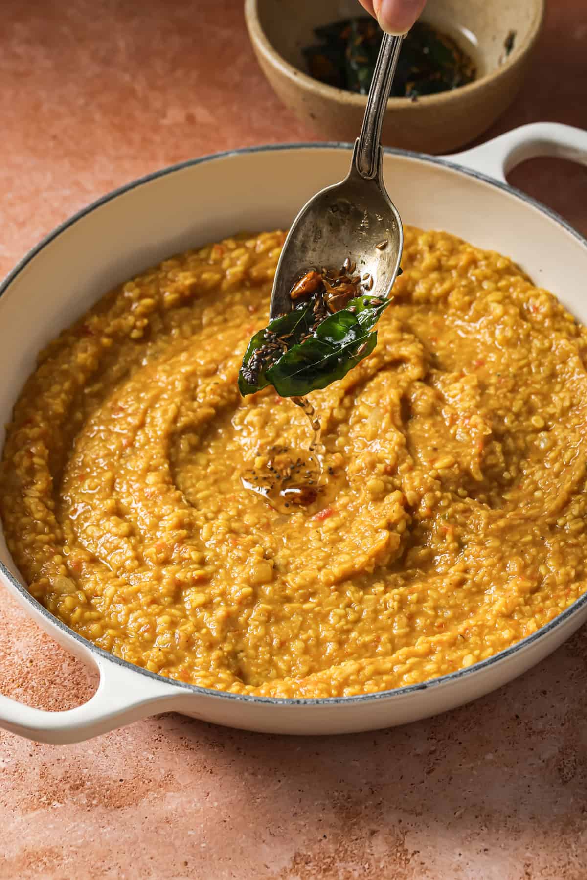 person spooning tadka over dal in deep saucepan.