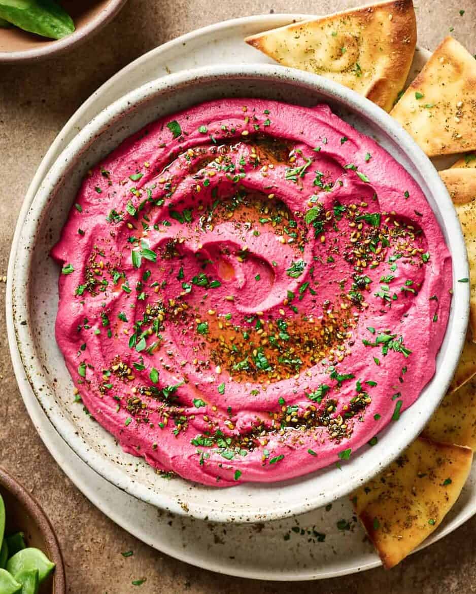 Bowl of beet hummus on a plate with pita bread.