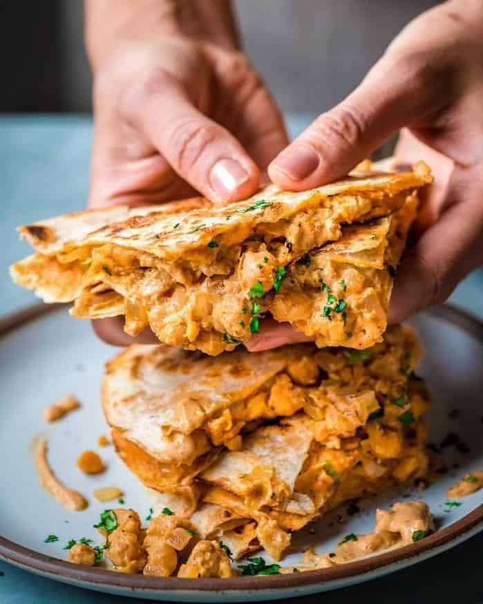 Woman holding a quarter of a buffalo chickpea quesadila over a plate with the rest of the quesadilla.