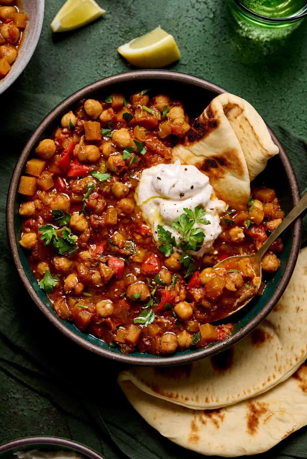 bowl of vegan tagine with chickpeas topped with yogurt and pita.
