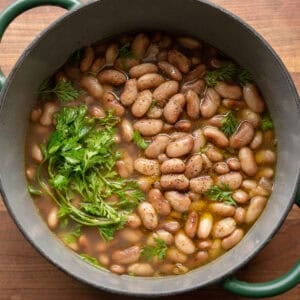 pot of brothy beans in a green saucepan on a wooden cutting board.