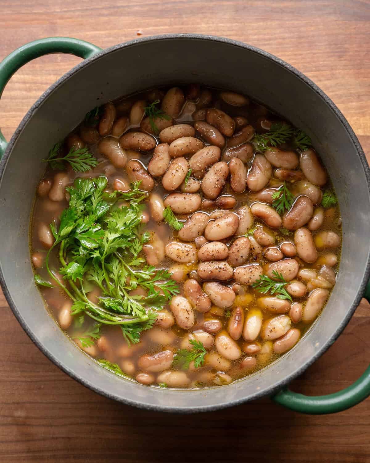 pot of brothy beans in a green saucepan on a wooden cutting board.