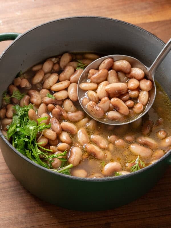 ladling brothy beans into a green saucepan on a wooden table.