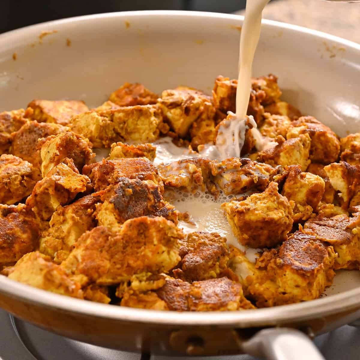 person pouring soy milk into pan with cooked tofu.