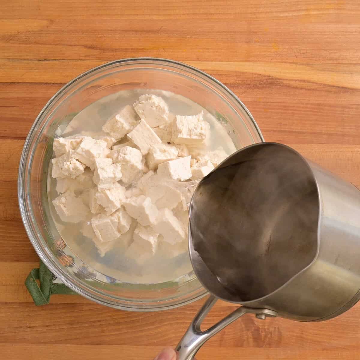 person pouring boiling water over tofu in the bowl.