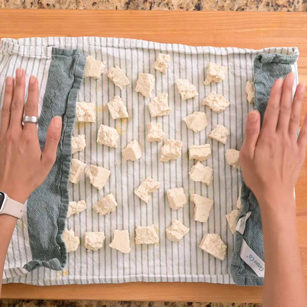 person patting off tofu with a dish towel.