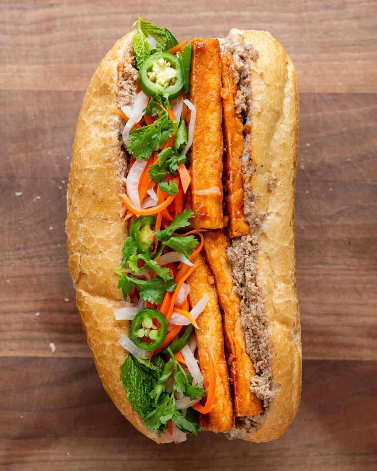 tofu banh mi loaded with toppings on a wooden cutting board.