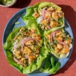 three thai laab salad lettuce cups on a plate next to a small bowl of chilis.