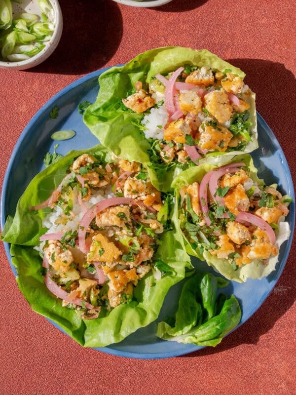 three thai laab salad lettuce cups on a plate next to a small bowl of chilis.