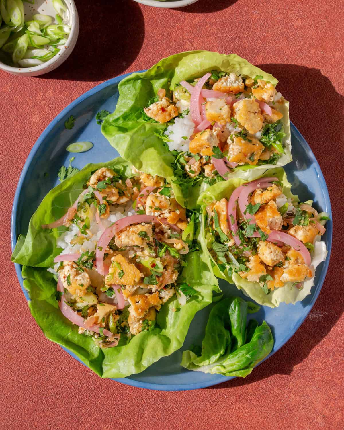 three thai laab salad lettuce cups on a plate next to a small bowl of chilis.