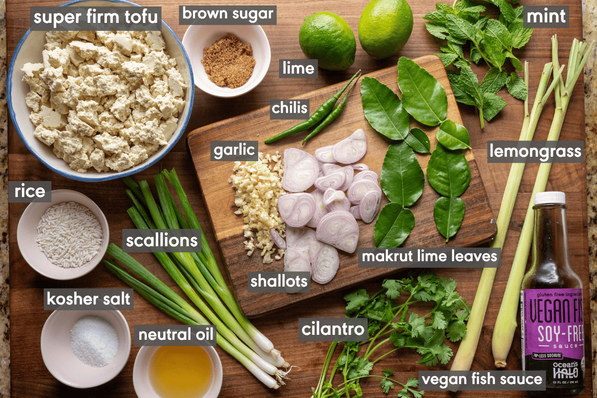 thai laab salad ingredients in small bowls on a wooden cutting board.