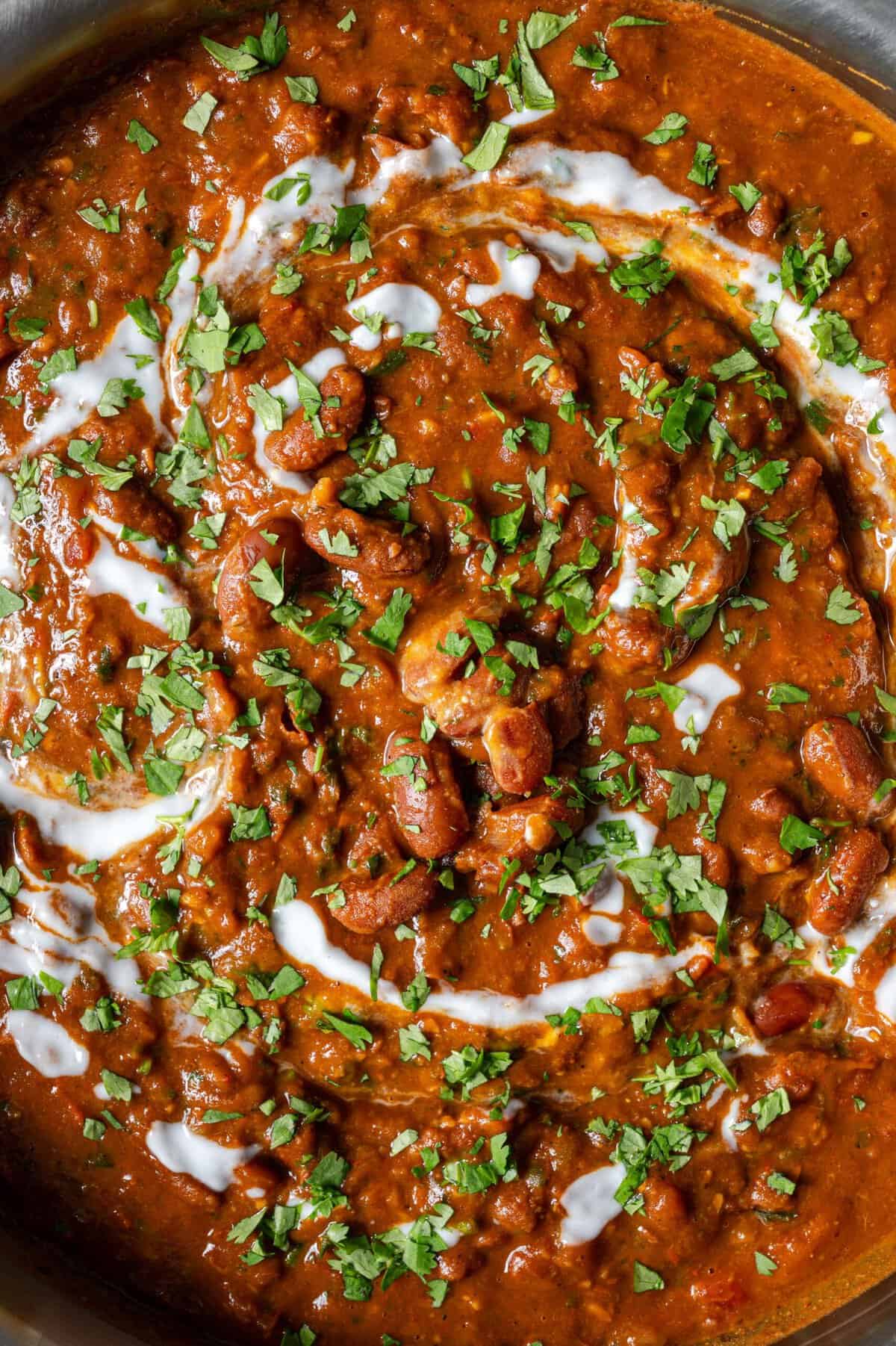 close up overhead view of rajma masala topped with yogurt, tadka and cilantro.